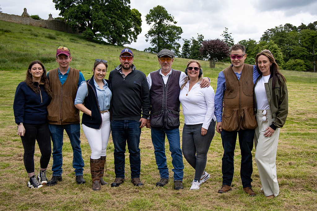 A smiling group of men and women pose in a country setting.