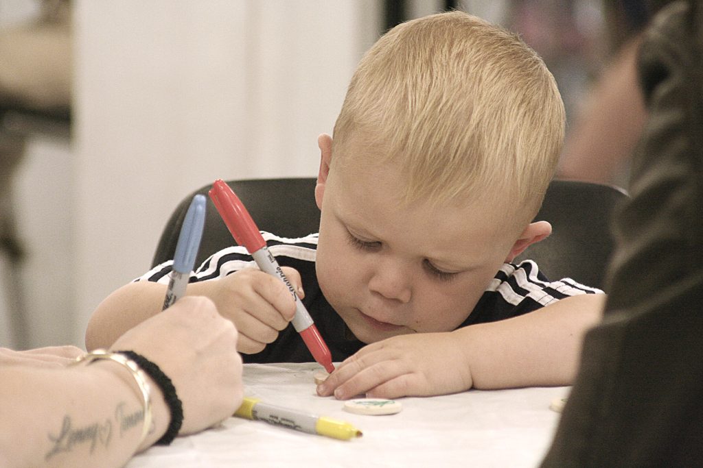 A small white boy concentrates as he draws on paper with a red marker.