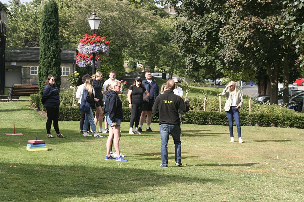 A team of colleagues receive instructions in a picturesque green setting with trees, plants and grass surrounding them.