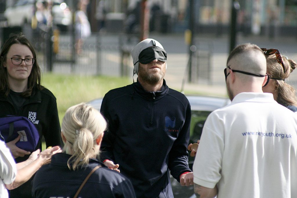 Team members stand, blindfolded, awaiting instructions.