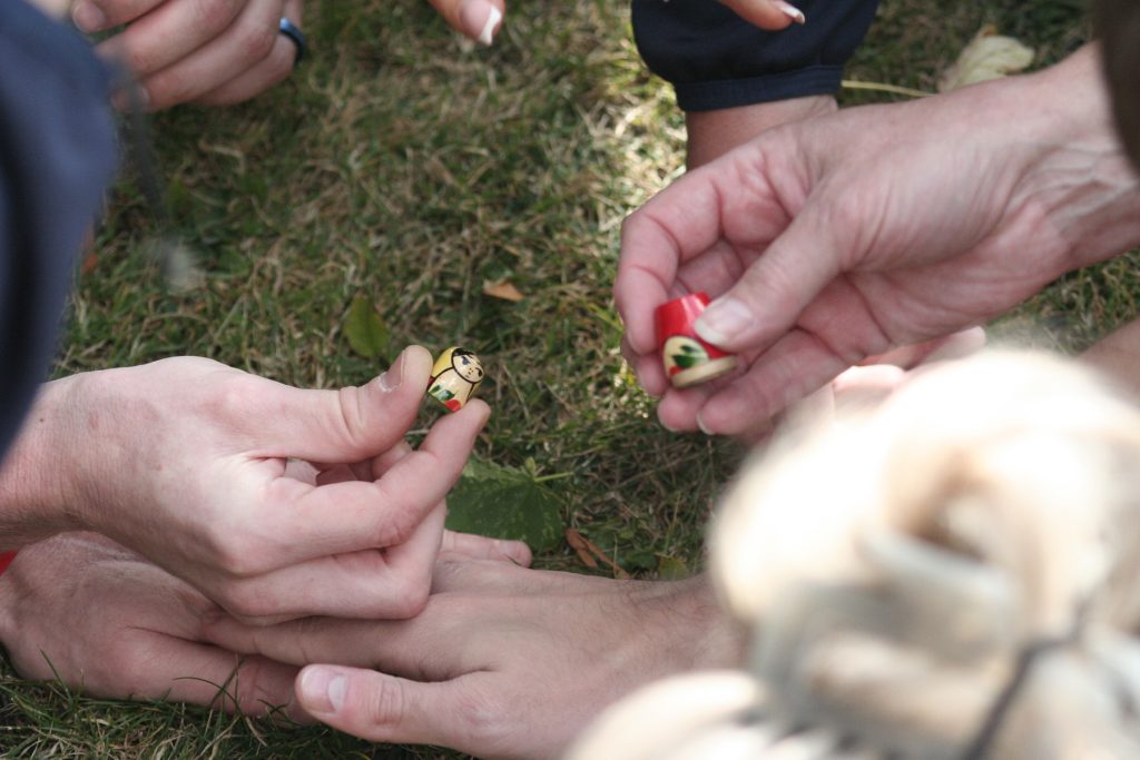 Hands are visible close up, holding two small parts of a Russian Doll in a blindfolded team-building task.