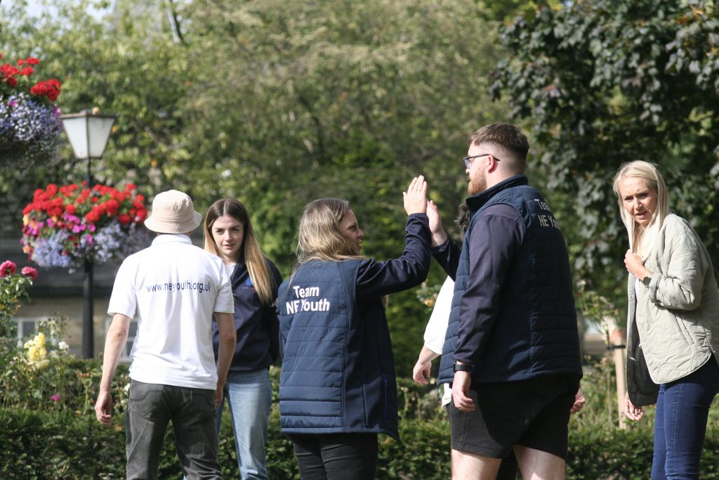 One white male and one white female high-five to the backdrop of a green park.