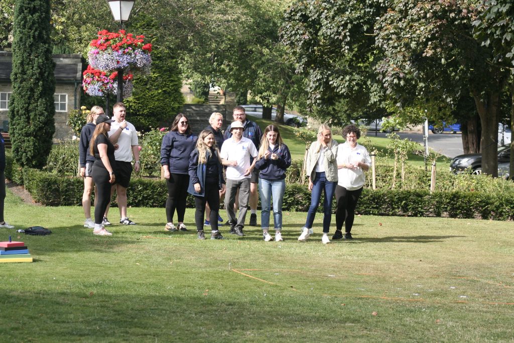 A team of colleagues await instructions in a picturesque green setting with trees, plants and grass surrounding them.