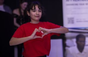 Young girl makes a heart shape with her hands during a performance at the 2025 NE Youth Impact Awards