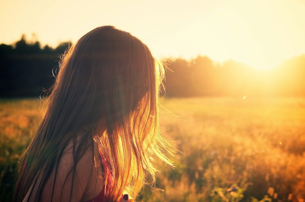 Young teen girl is silhouetted by a warm summer sun as it begins to set